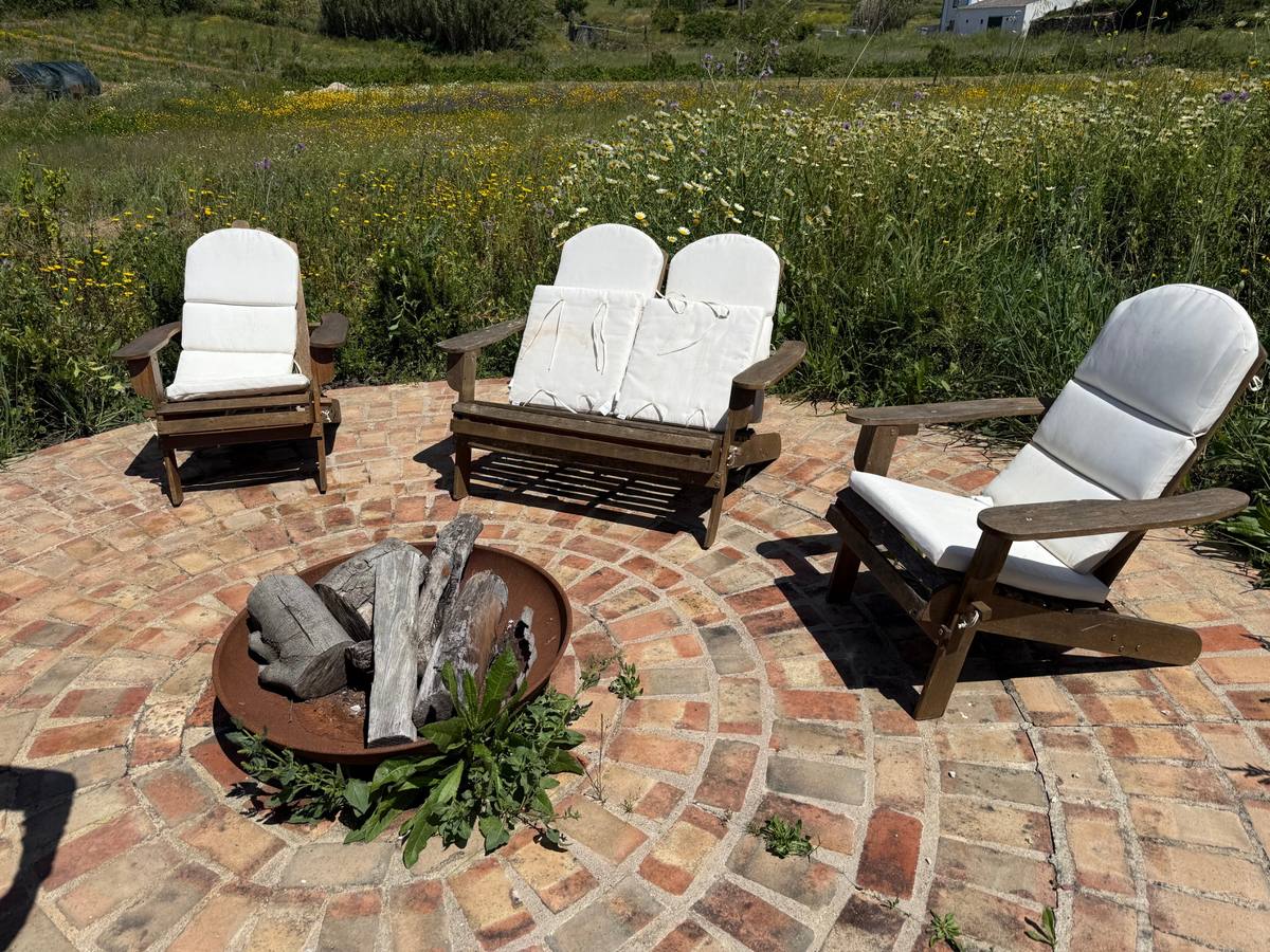 Wooden chairs around a fire pit on a round brick terrace, with a wildflower meadow behind